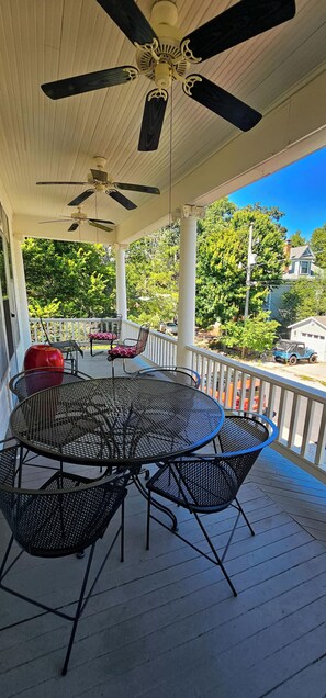 A covered outdoor patio with a round metal table and chairs, a ceiling fan, and a view of a residential street. - Historic Bed & Breakfast 8 Bedrooms, Groups/family (Eureka Springs)