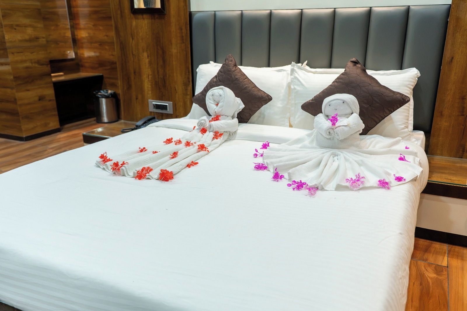 A hotel room with a neatly made bed, a wooden headboard, and a small bedside table with a lamp.