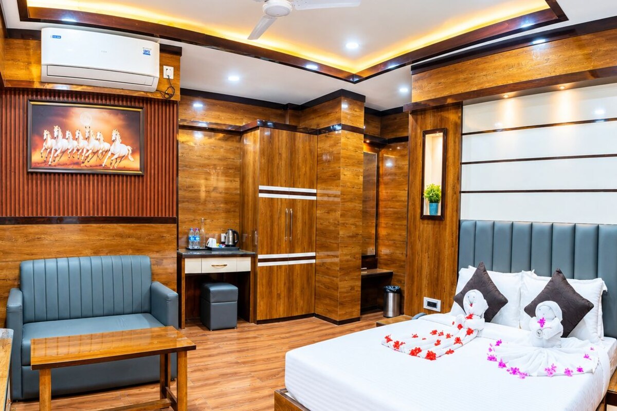 A hotel room with a wooden floor, a bed with a white bedspread, a sofa, a desk, and a ceiling fan.
