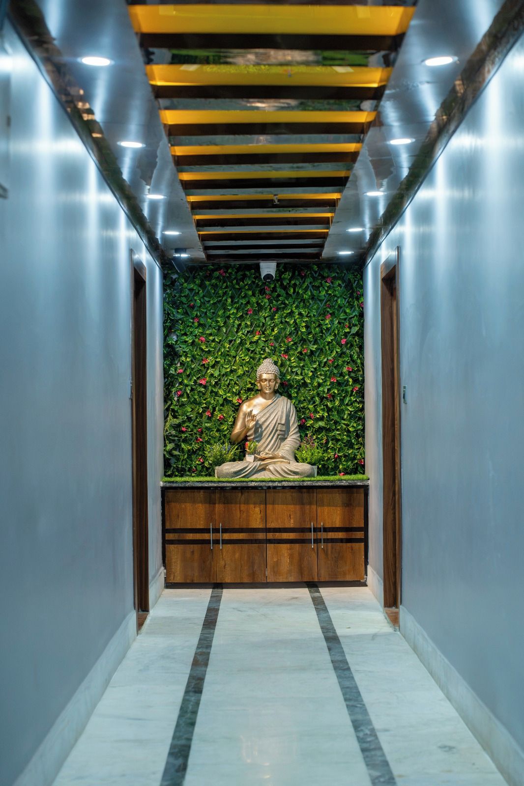 A statue of a seated figure in a corridor with a green leafy wall and a wooden bench.
