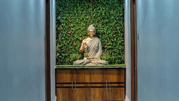 A statue of a seated figure in a corridor with a green leafy wall and a wooden bench.