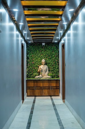 Una estatua de una figura sentada en un pasillo con un muro cubierto de hojas verdes y un banco de madera.