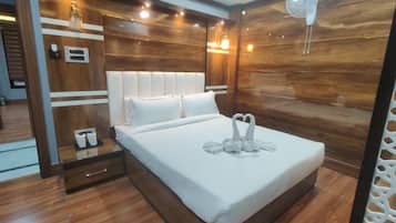 Une chambre d’hôtel moderne avec une tête de lit en bois, un lit avec du linge de maison blanc, une table de chevet avec une lampe et un ventilateur fixé au mur.
