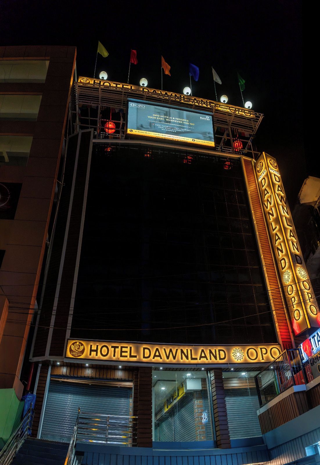 A hotel facade with a marquee sign, multiple flags, and a large illuminated sign advertising the hotel.