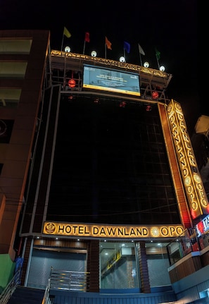 Fachada de hotel con un cartel luminoso, varias banderas y un gran anuncio iluminado que anuncia el hotel.