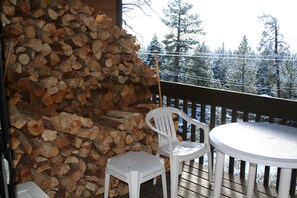 Una terraza de madera con un muro de piedra, dos sillas blancas de plástico y una mesa redonda.