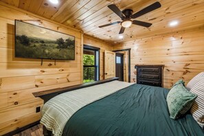 Ein Schlafzimmer mit Holzvertäfelung, einem Bett, einem Deckenventilator, einem Schminktisch und einem Bild an der Wand.