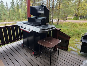 A barbecue grill on an outdoor deck with a wooden railing and a view of a forested area. - Orrenkolo Cabin, in Luosto, Finnish Lapland (Luosto)