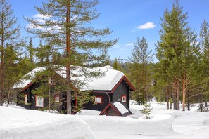 Una cabaña con techo nevado, rodeada de árboles y nieve.