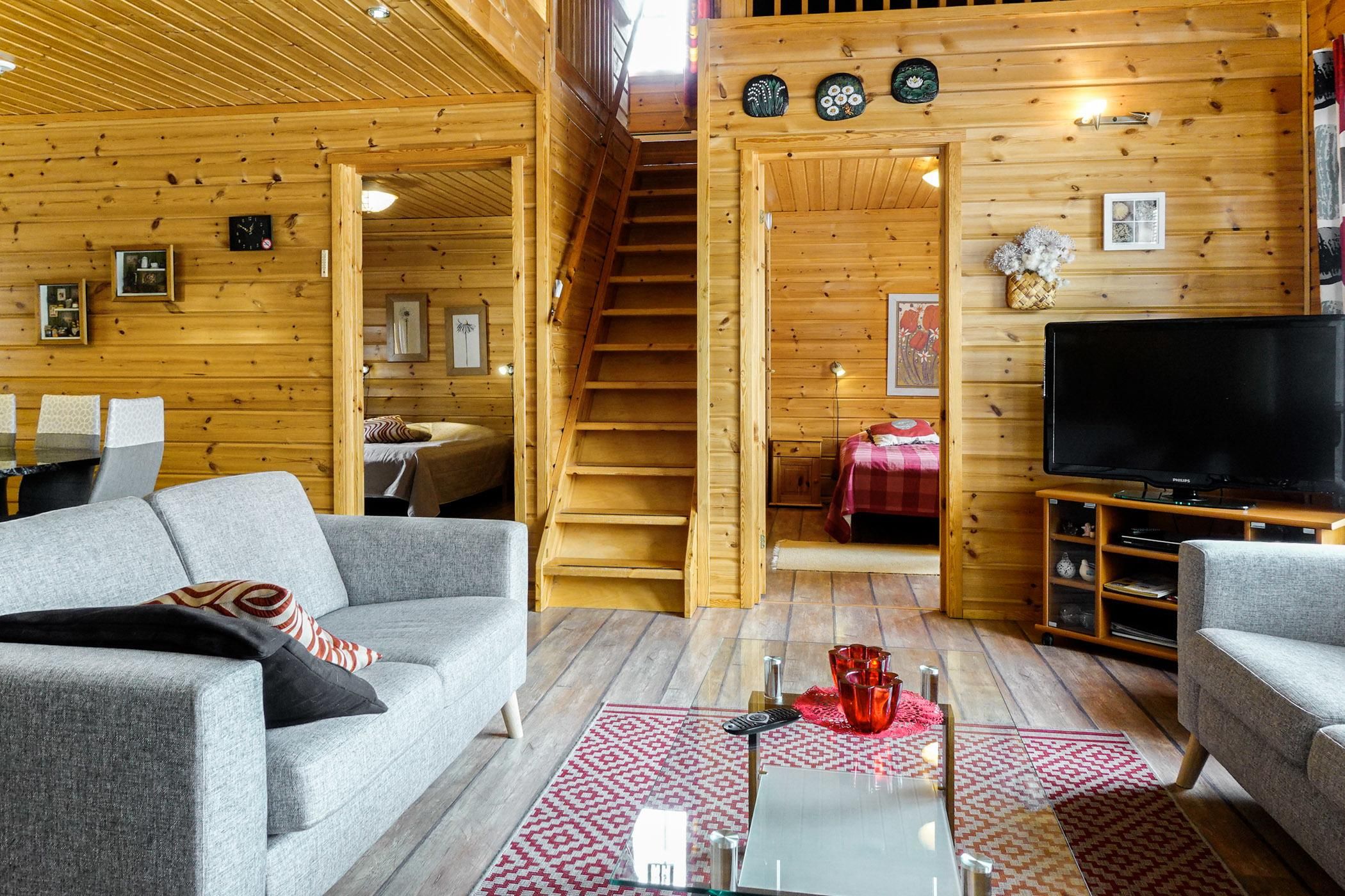 A wooden interior with a sofa, a TV, and a staircase leading to another room.
