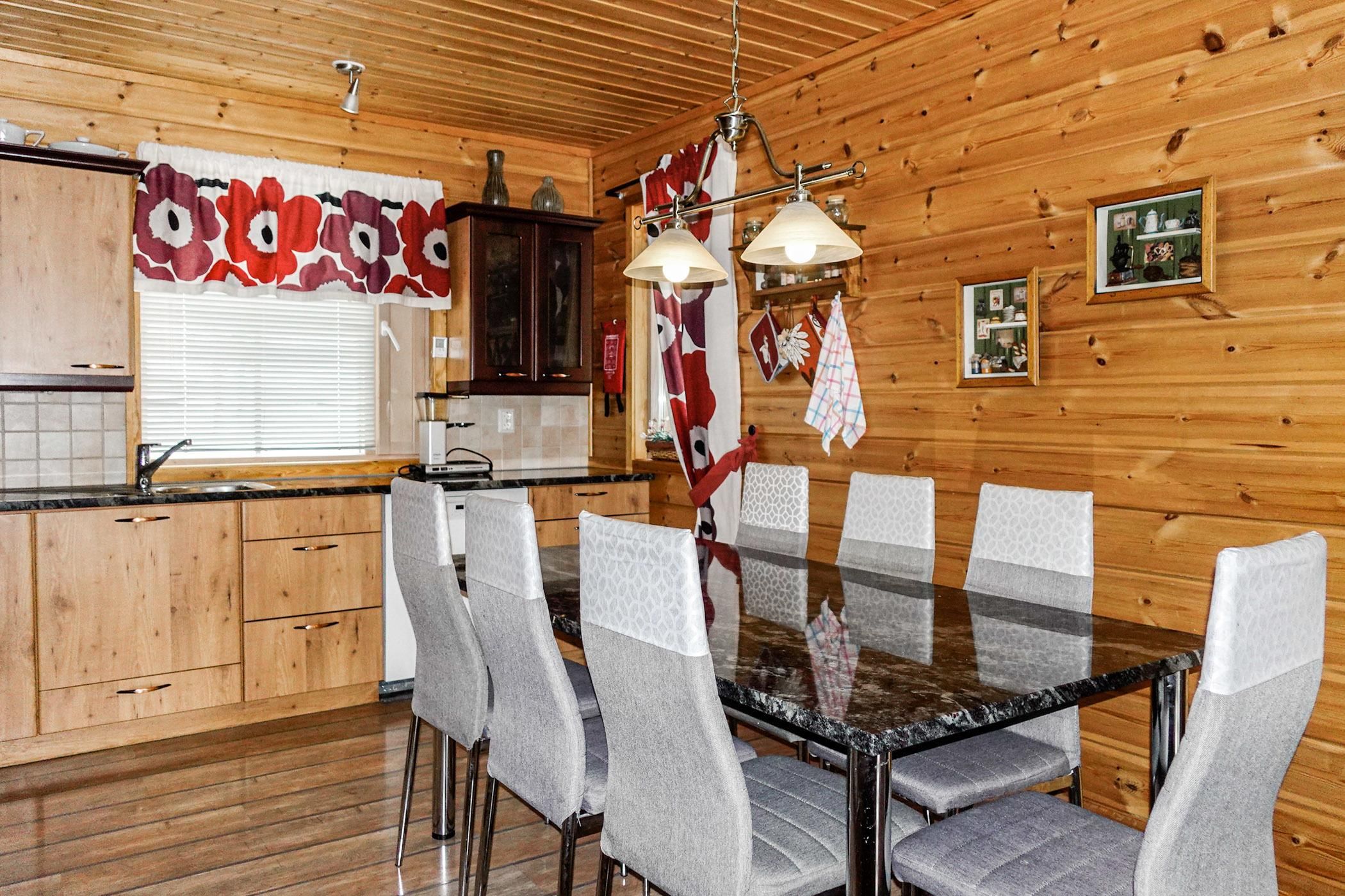Un interior de madera con una mesa de comedor, sillas, una zona de cocina y una lámpara de techo.