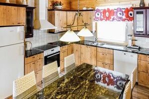 A kitchen with wooden cabinets, a black countertop, a stove, a sink, and pendant lighting. - Orrenkolo Cabin, in Luosto, Finnish Lapland (Luosto)