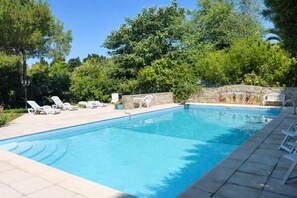 Ein rechteckiger Swimmingpool mit Steinmauer und Wandgemälde, umgeben von Liegestühlen und Grünpflanzen.