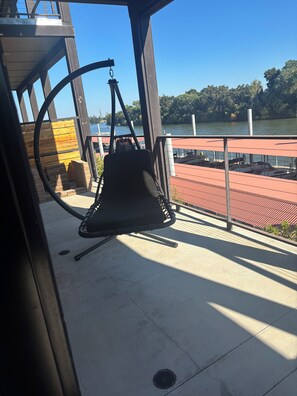 A swing chair on a balcony overlooking a body of water with a dock and boats. - Riverview luxury master suite only 13 minutes from the Sac International Airport (Sacramento)