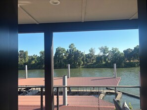 A view from inside a building with large windows overlooking a dock and a body of water, with trees and a clear sky in the background. - Riverview luxury master suite only 13 minutes from the Sac International Airport (Sacramento)