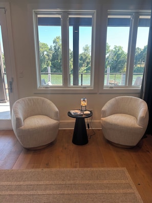 A room with two armchairs, a small table with a lamp, and large windows overlooking a body of water. - Riverview luxury master suite only 13 minutes from the Sac International Airport (Sacramento)