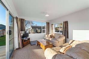 Ein geräumiges Wohnzimmer mit einem großen Flachbildfernseher, einem beige-farbenen Sofa und einem Holztisch.