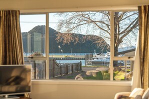Ein Zimmer mit einem großen Fenster mit Blick auf einen Yachthafen, wo Boote und eine Anlegestelle zu sehen sind, mit einem Berg im Hintergrund.