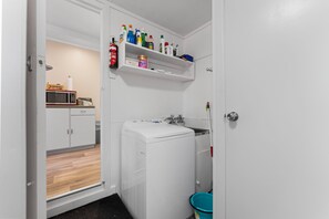 A compact laundry room with a washing machine, a drying rack, and a shelf with cleaning supplies. - The Little Jetty - Motuoapa Holiday Home (Motuoapa)