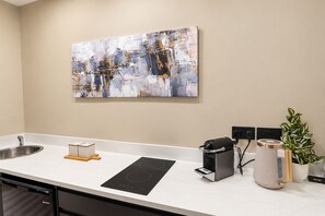 Une cuisine moderne avec un évier en acier inoxydable, une plaque de cuisson à induction noire, une machine à café et une plante en pot.