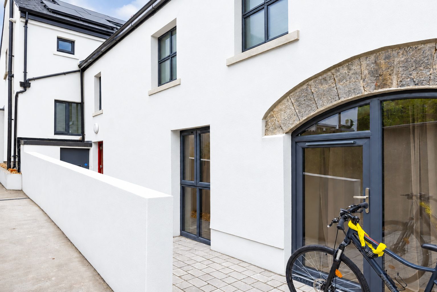 A modern building with a white exterior, a stone archway, and a bicycle parked outside.