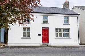 Un bâtiment à deux étages avec une porte rouge, des murs blancs et de nombreuses fenêtres.