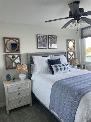 A bedroom with a bed, nightstands, a ceiling fan, wall art, and a window with a view. - Luxury Waterfront Condo in Clearwater Beach 3 bedroom 3 full bath (Clearwater)