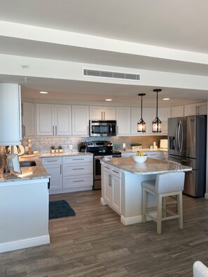 A modern kitchen with white cabinetry, stainless steel appliances, a granite countertop, and pendant lighting. - Luxury Waterfront Condo in Clearwater Beach 3 bedroom 3 full bath (Clearwater)