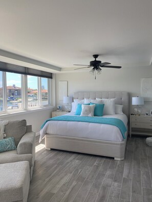 A bedroom with a large bed, a ceiling fan, a nightstand, and a view of the outside. - Luxury Waterfront Condo in Clearwater Beach 3 bedroom 3 full bath (Clearwater)