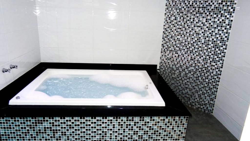A rectangular hot tub with a black edge, surrounded by white tiled walls and a mosaic tile border.