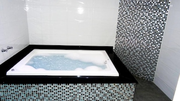 Una bañera de hidromasaje rectangular con borde negro, rodeada de paredes de azulejos blancos y un borde de mosaicos.
