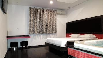 Een hotelkamer met een bed, een zithoekje, een raam met gordijnen en een bad.