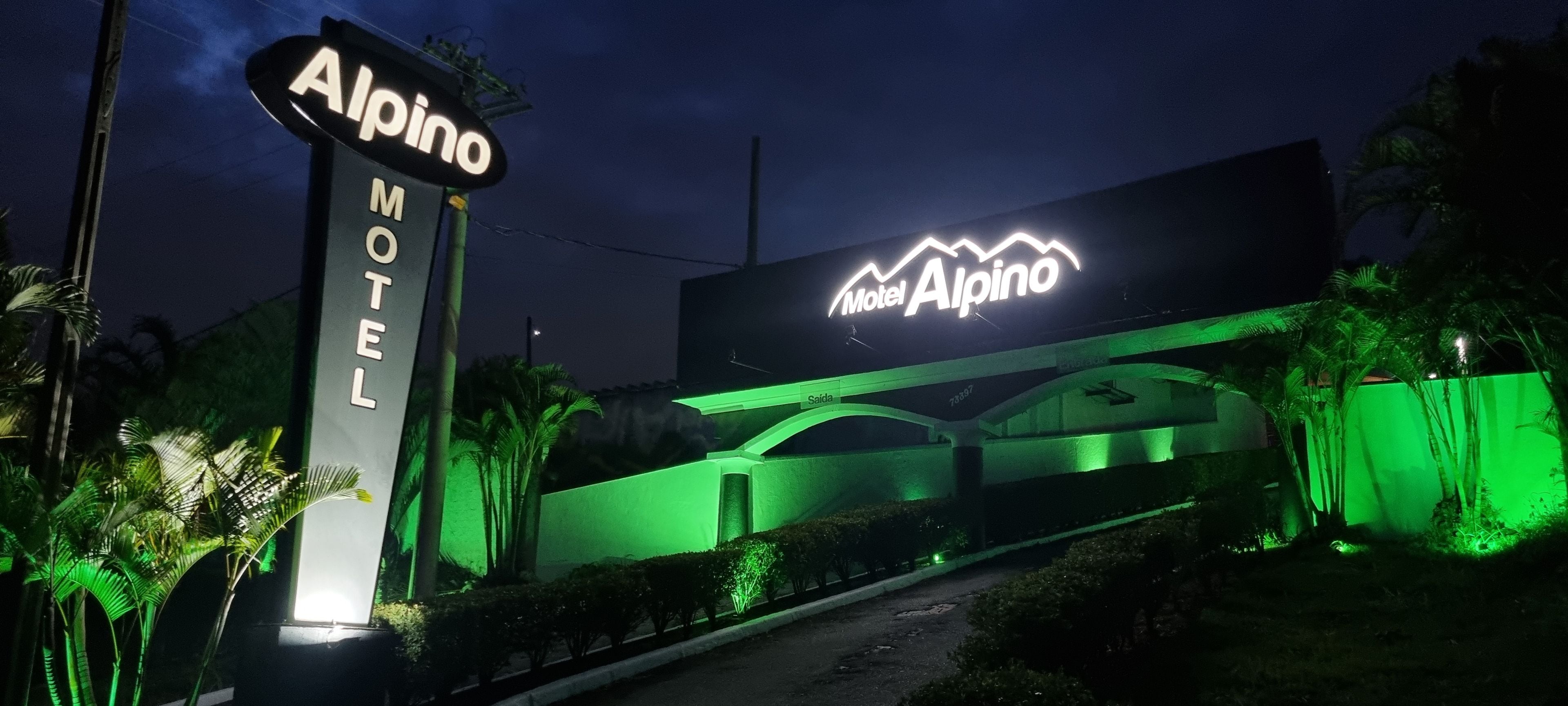 A motel sign with 'Alpino' and 'Motel Alpino' text, a green-lit entrance, and a parking area.