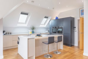A modern kitchen with a central island, two bar stools, and a skylight. - Luxury 2-Bed Coastal Apartment with Sea Views, Balcony & Dedicated Parking (Worthing)