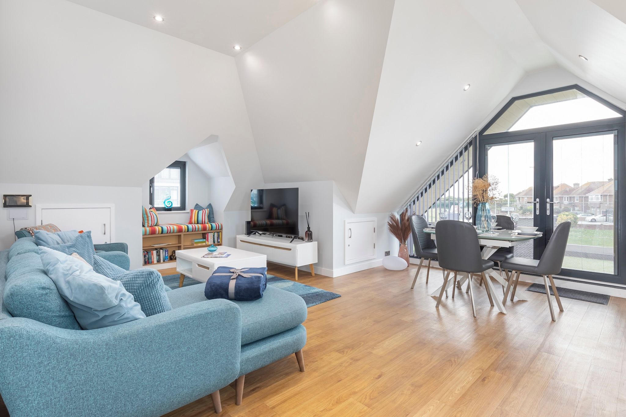 A spacious loft with a high ceiling, a cozy seating area, a dining space, and a large window offering a view.