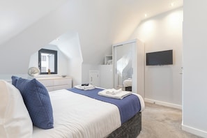 A bedroom with a bed, a dresser, a mirror, a wardrobe, and a television. - Luxury 2-Bed Coastal Apartment with Sea Views, Balcony & Dedicated Parking (Worthing)
