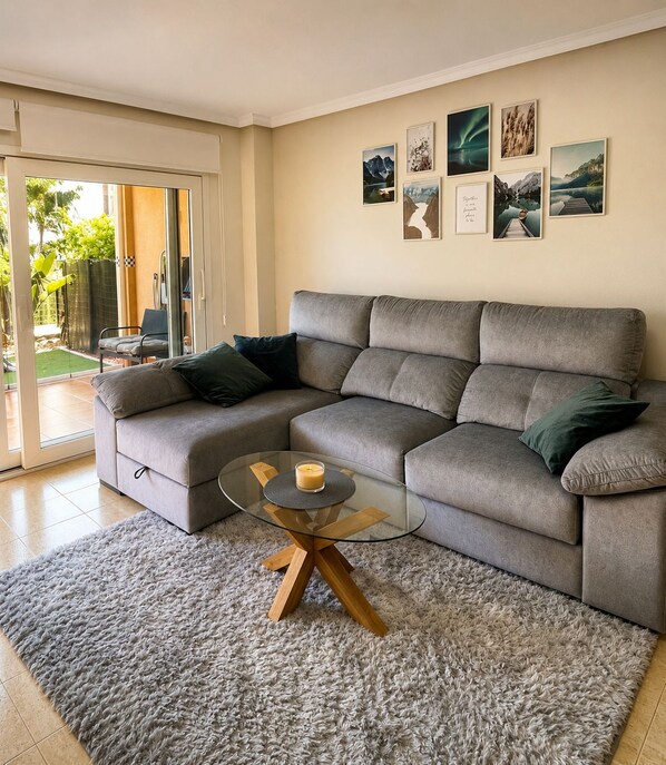 En moderne stue med en grå hjørnesofa, et glasbord og en grå, lurvet måtte.