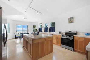 A modern kitchen with a central island, wooden cabinets, a built-in oven, and a view of the ocean. - Cielo y Mar Beach House | Direct Beach Access (Humacao)