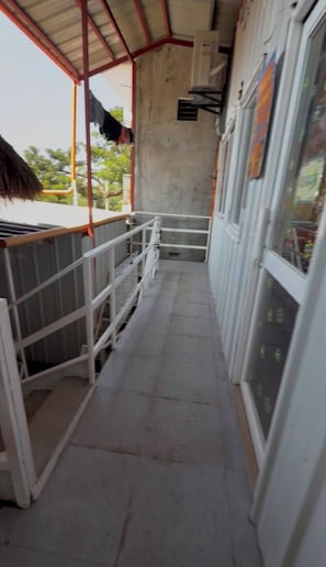 Un couloir étroit avec une rambarde métallique, un sol en béton et l’entrée d’un immeuble dotée de portes en verre.