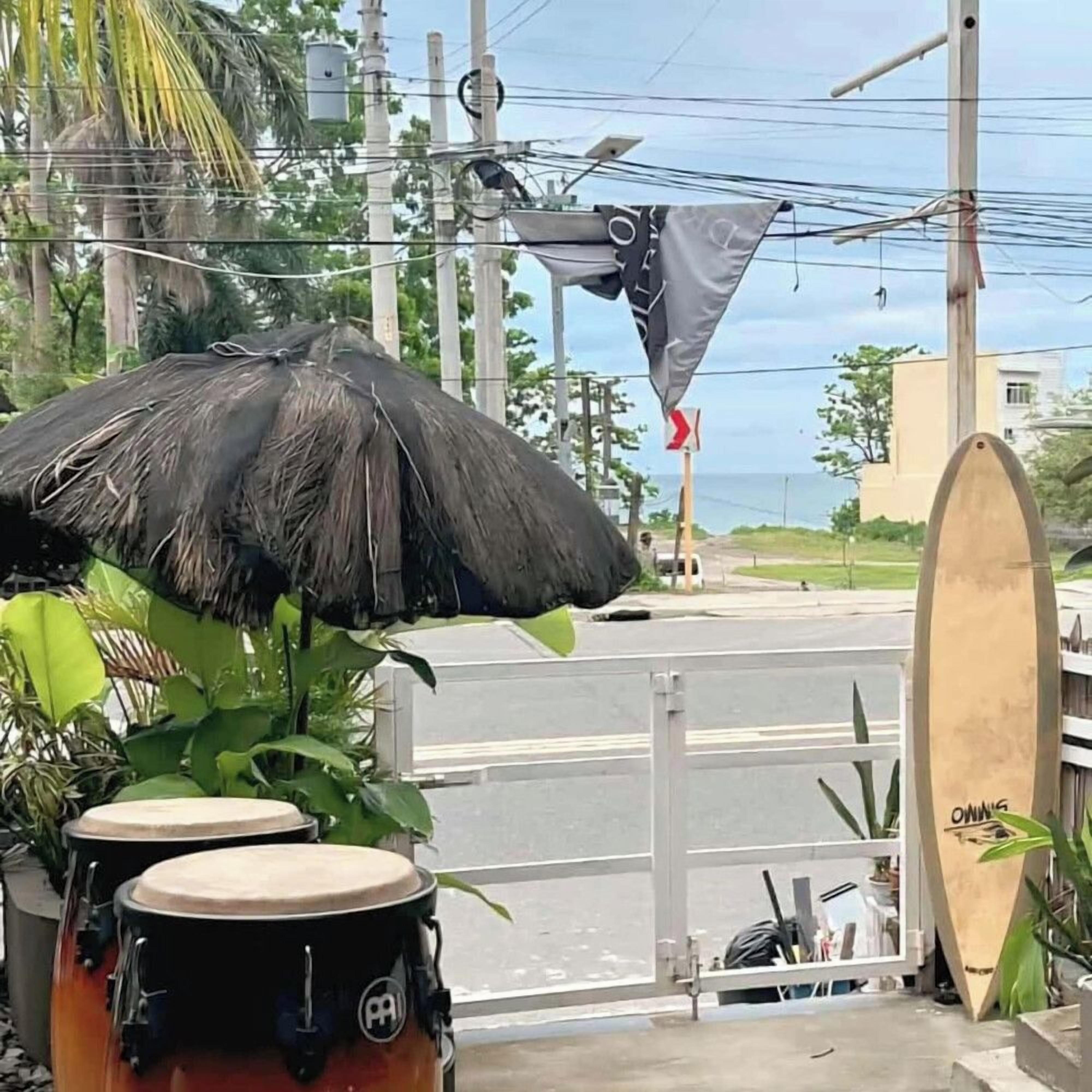 Une scène de rue avec un parasol en chaume, une planche de surf et un panneau de signalisation.