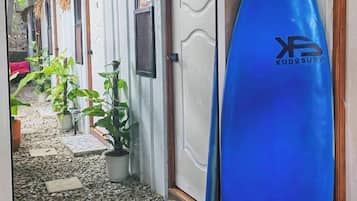 Een gang met potplanten, een surfplank en een deur met een reliëfpatroon.