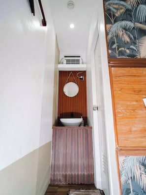 Un couloir étroit avec une porte en bois sur la droite, un mur blanc et une petite fenêtre avec un cadre en bois.