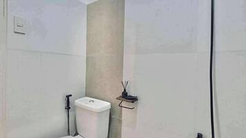 A small bathroom with a toilet, a shower, and a waste bin.