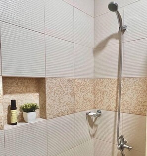 A bathroom with a shower, a sink, and a shelf with a plant and a bottle. - Little Garden Home | Garden View (Parañaque)
