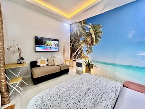 A bedroom with a large bed, a sofa, a TV, and a mural of a beach scene. - Little Garden Home | Garden View (Parañaque)
