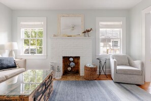 Un salon avec une cheminée en briques blanches, un canapé, un fauteuil et une table basse.