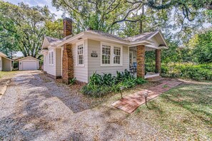 Une petite maison de plain-pied avec une cheminée en briques, un porche à l’avant et une allée gravillonnée.