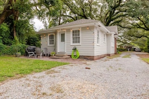 A small single-story house with a porch, a lawn, and a gravel driveway. - Quaint little cottage nestled in the heart of East Hill! (Pensacola)