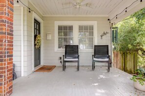Une véranda avec deux chaises en bois, une porte blanche et une fenêtre avec des stores.