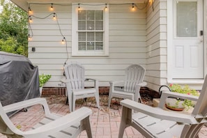 An outdoor patio with two Adirondack chairs, a small table, and string lights. - Quaint little cottage nestled in the heart of East Hill! (Pensacola)